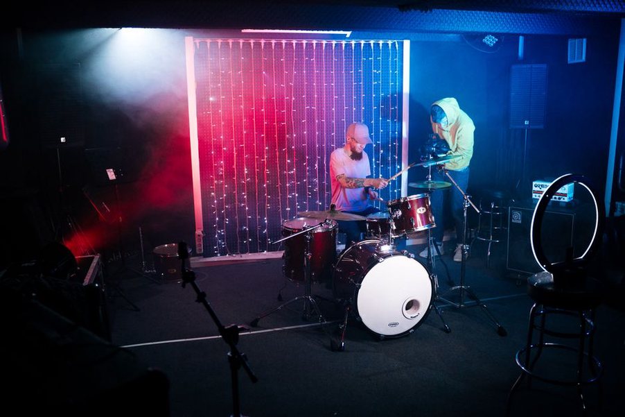 A camera operator films a drummer on a compact stage