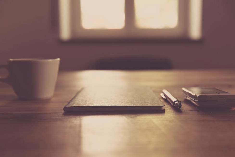 A notebook beside a cup on a clear desk